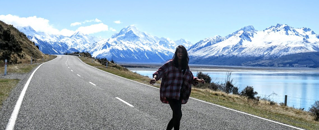 female student is happy and smiling on a road leading into the mountains of New Zealand